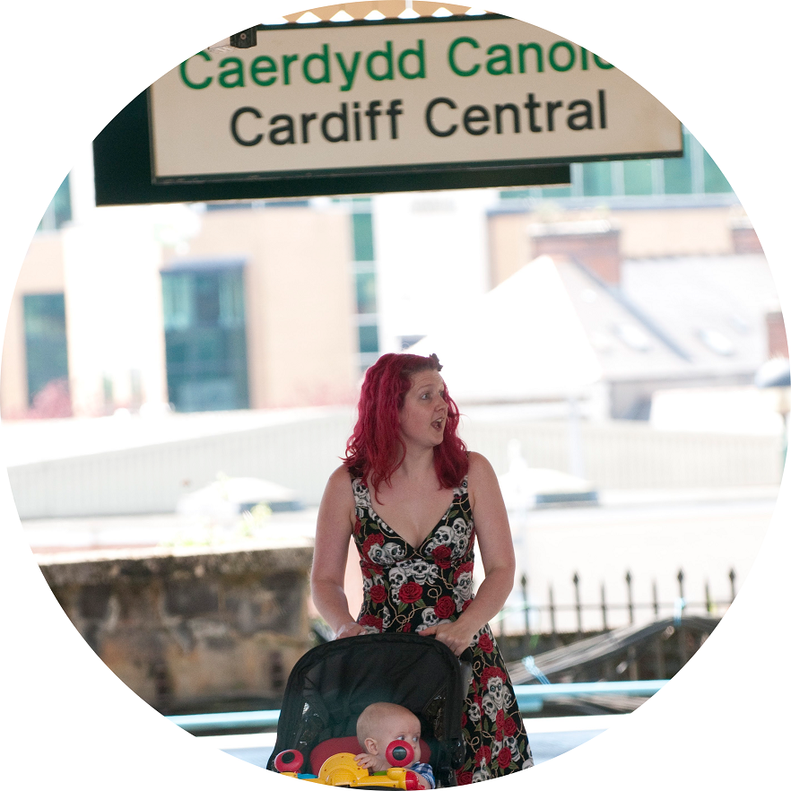 A woman pushing a buggy underneath the bilingual Cardiff Central sign