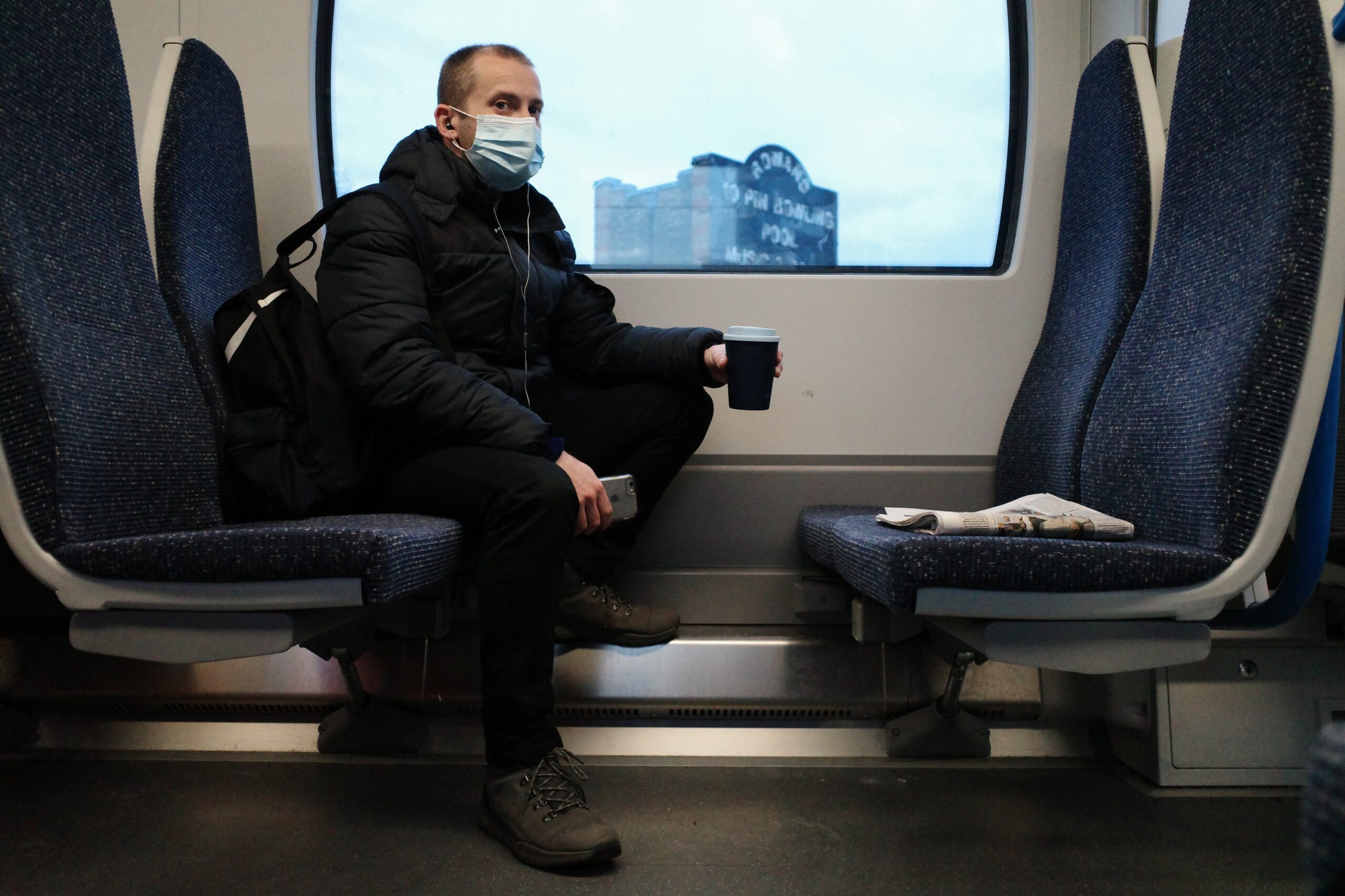 man on train in facemask holding coffee