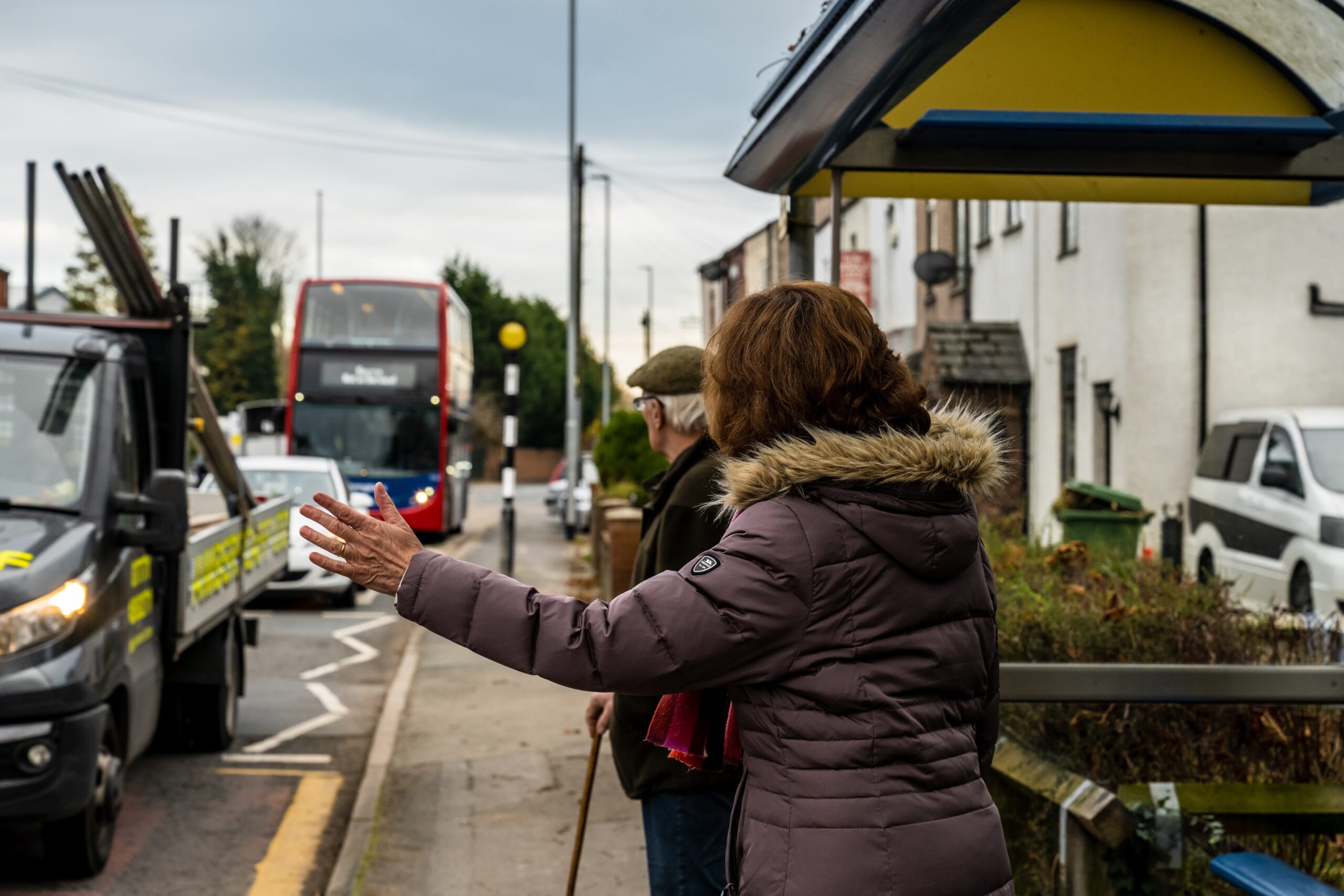 woman at bus stop with arm out to flag approaching bus