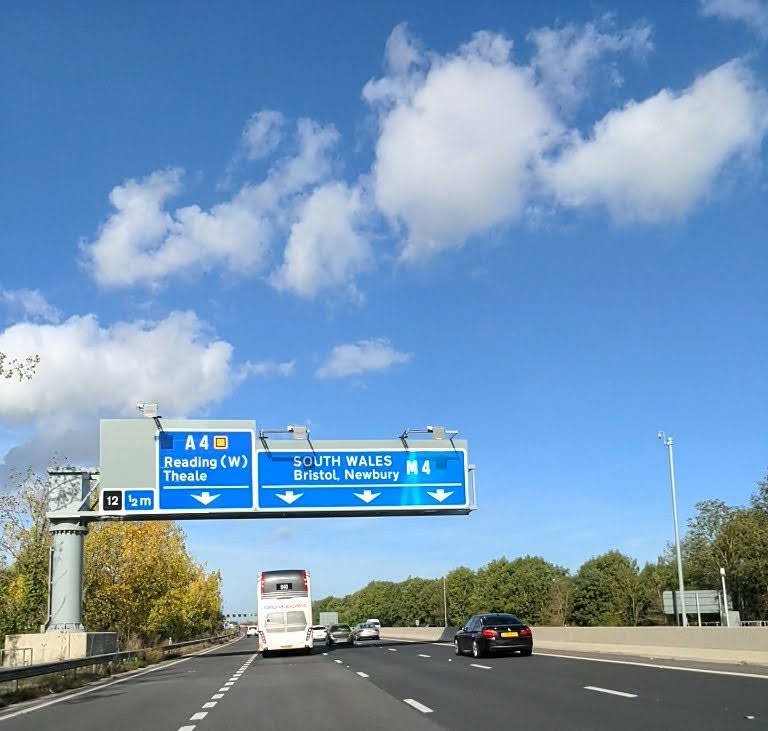 Coach and car passing under overhead signage on motorway