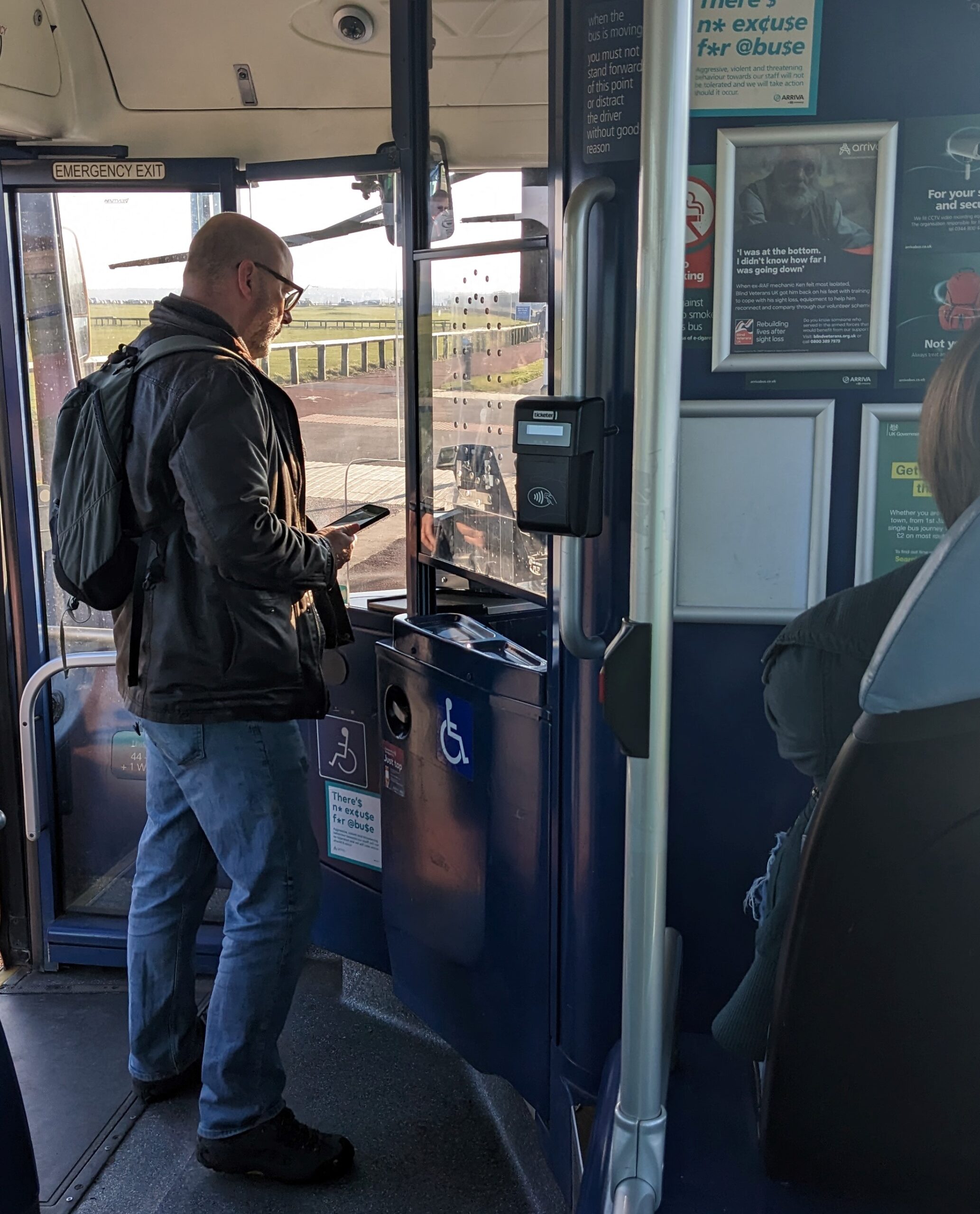 white man in glasses standing by bus driver paying with phone