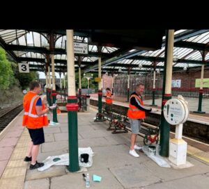 People painting green pillars at a train station