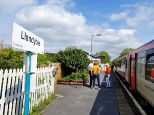 People waiting on a platform at near a sign which says Llandybie station